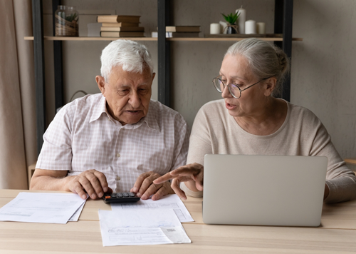 Image of a senior woman caring for a parent or spouse sitting at the kitchen table looking at bills